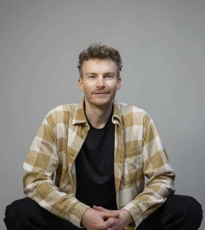 René Margull – Agile Coach und Experte für digitale Transformation, sitzt entspannt vor neutralem Hintergrund.